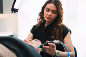 A female Erasable Med Spa provider wearing black scrubs slowly swipes the DiamondGlow's applicator over a female patient's cheek at our facial spa in Tampa.